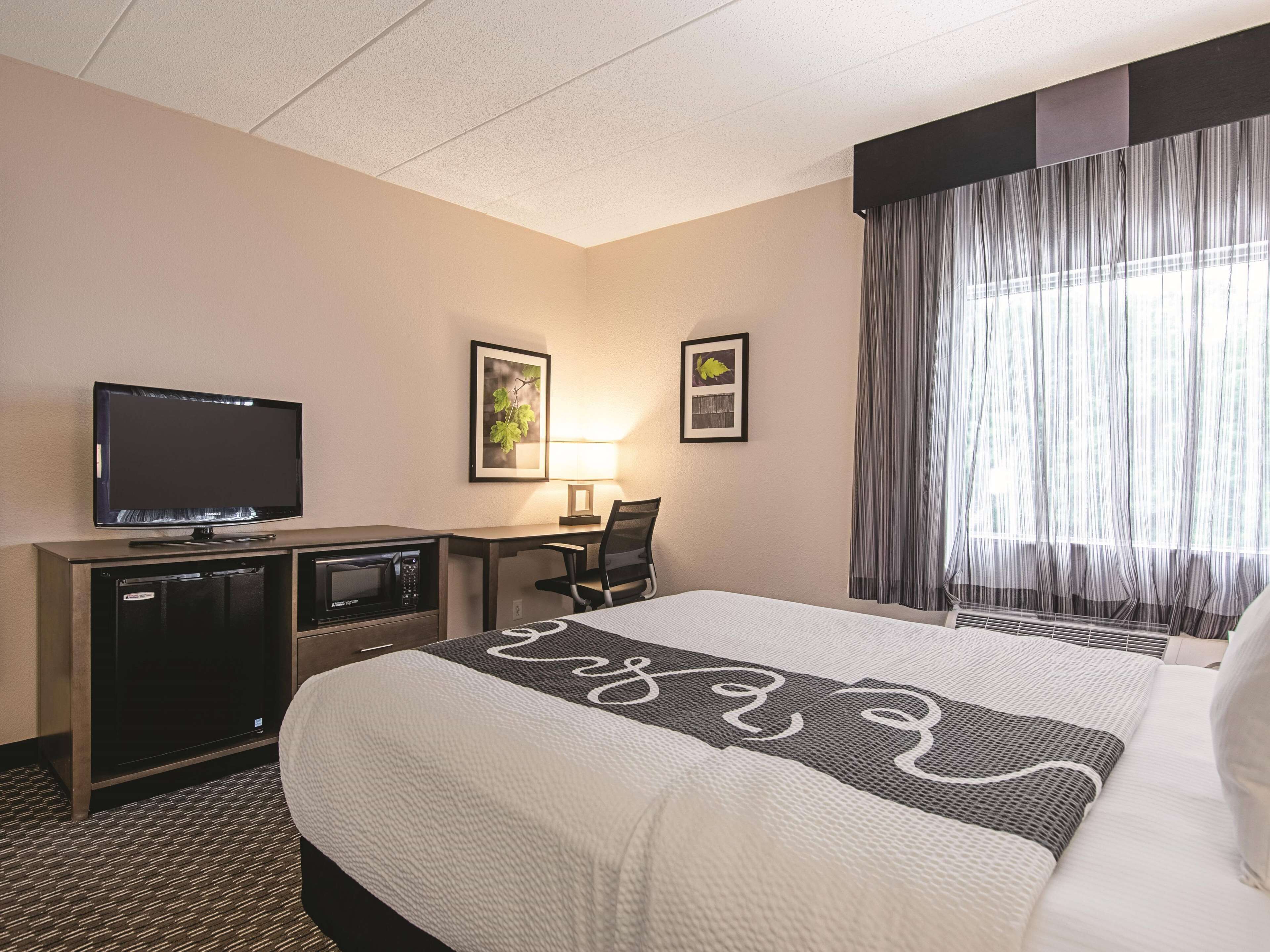 A hotel room with a bed, a desk, a television, a microwave, and a lamp.