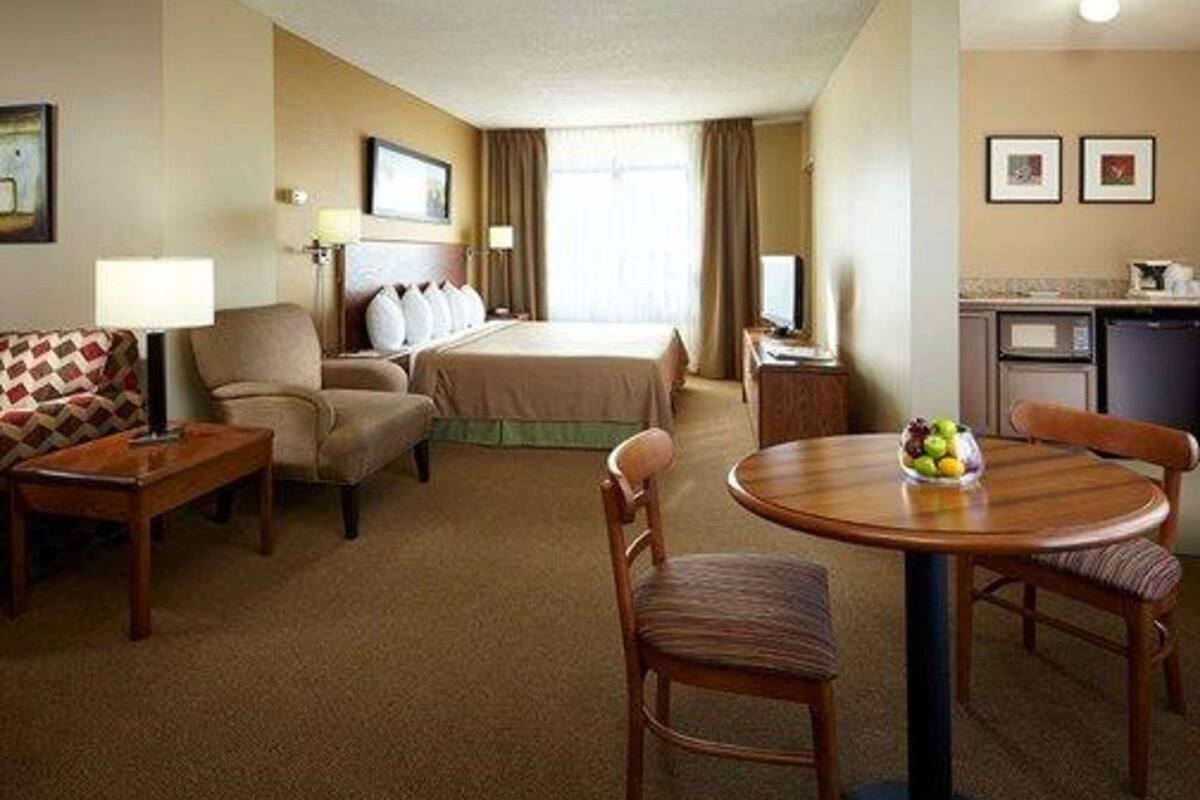 A hotel room with a bed, a sofa, a desk, a dining table with fruit, and a kitchenette.