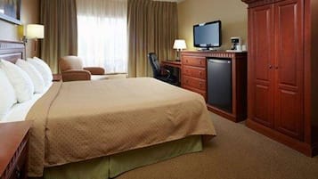 A hotel room with a large bed, a television, a desk with a computer, and a wardrobe.