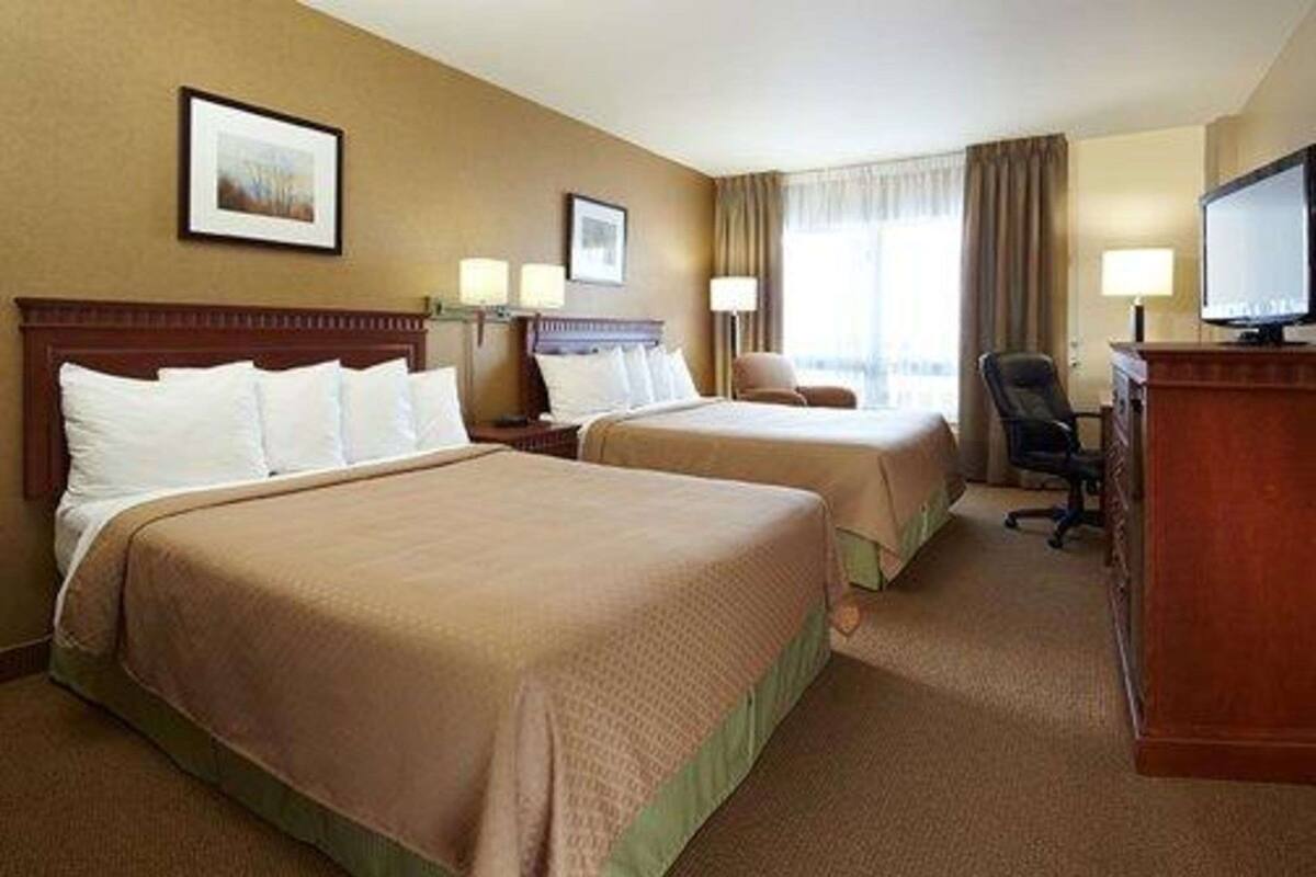 A hotel room with two beds, a desk, a chair, and a television.