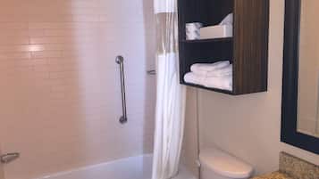A bathroom with a white bathtub, a toilet, a shower with a glass door, and a towel rack with folded towels.