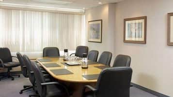 Un salón de conferencias con una larga mesa, sillas negras y cuadros en las paredes.