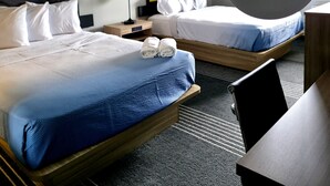 A hotel room with two beds, a desk, a chair, a lamp, and artwork on the walls.