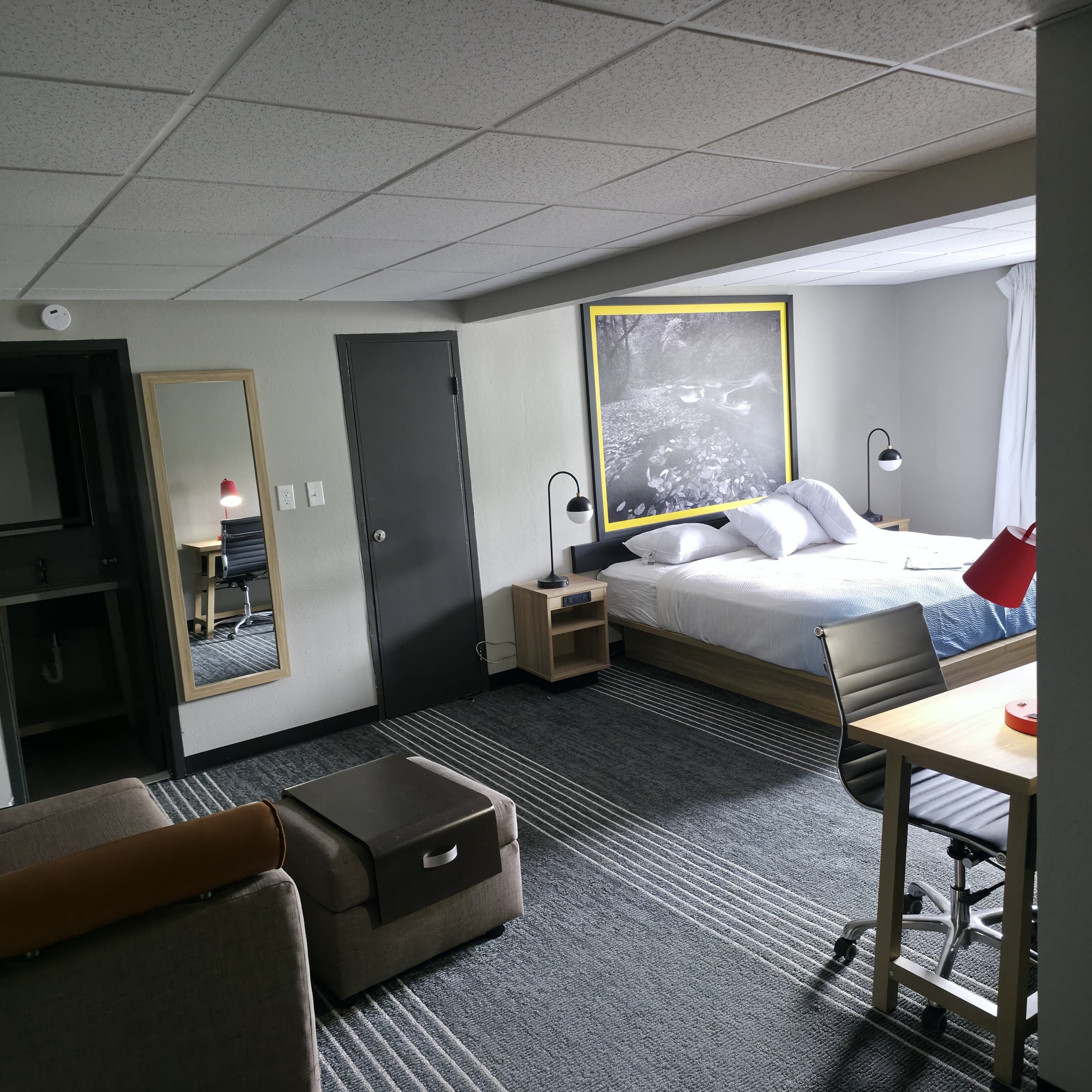 A hotel room with a bed, desk, chair, and a large mirror.