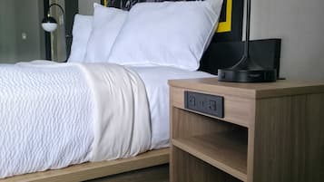 Una habitación de hotel con una cama, una mesita de noche con lámpara y un enchufe en la pared.