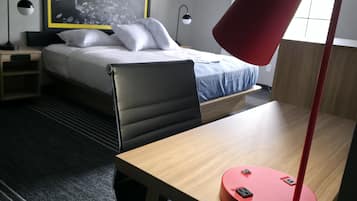 Una habitación de hotel con una cama, un escritorio con una lámpara roja, una silla y un ventanal grande.