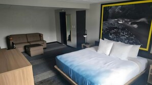 A hotel room with a bed, a sofa, a desk, and a large framed picture on the wall.
