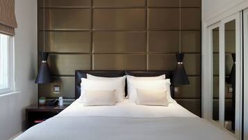 A neatly made bed with a headboard, bedside lamps, and a nightstand with a plant and a bottle.