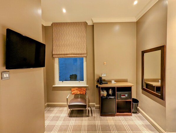Un baño con televisión montada en la pared, una ventana con vistas al exterior, un lavabo con espejo y un mueble pequeño con artículos de aseo.