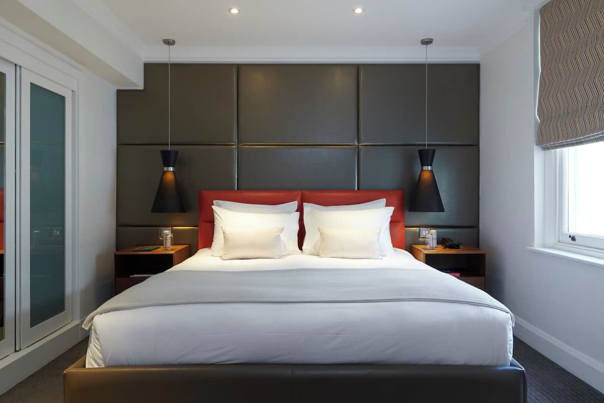 Una habitación de hotel moderna con una cama grande, dos mesitas de noche, un cabecero con paneles e iluminación colgante.