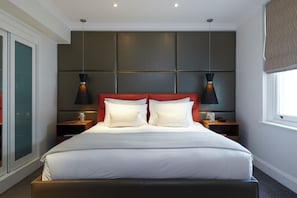 A modern hotel room with a large bed, two bedside tables, a headboard with panels, and pendant lighting.