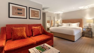 A hotel room with a large bed, a red sofa, a small table with a magazine, and framed artwork on the wall.