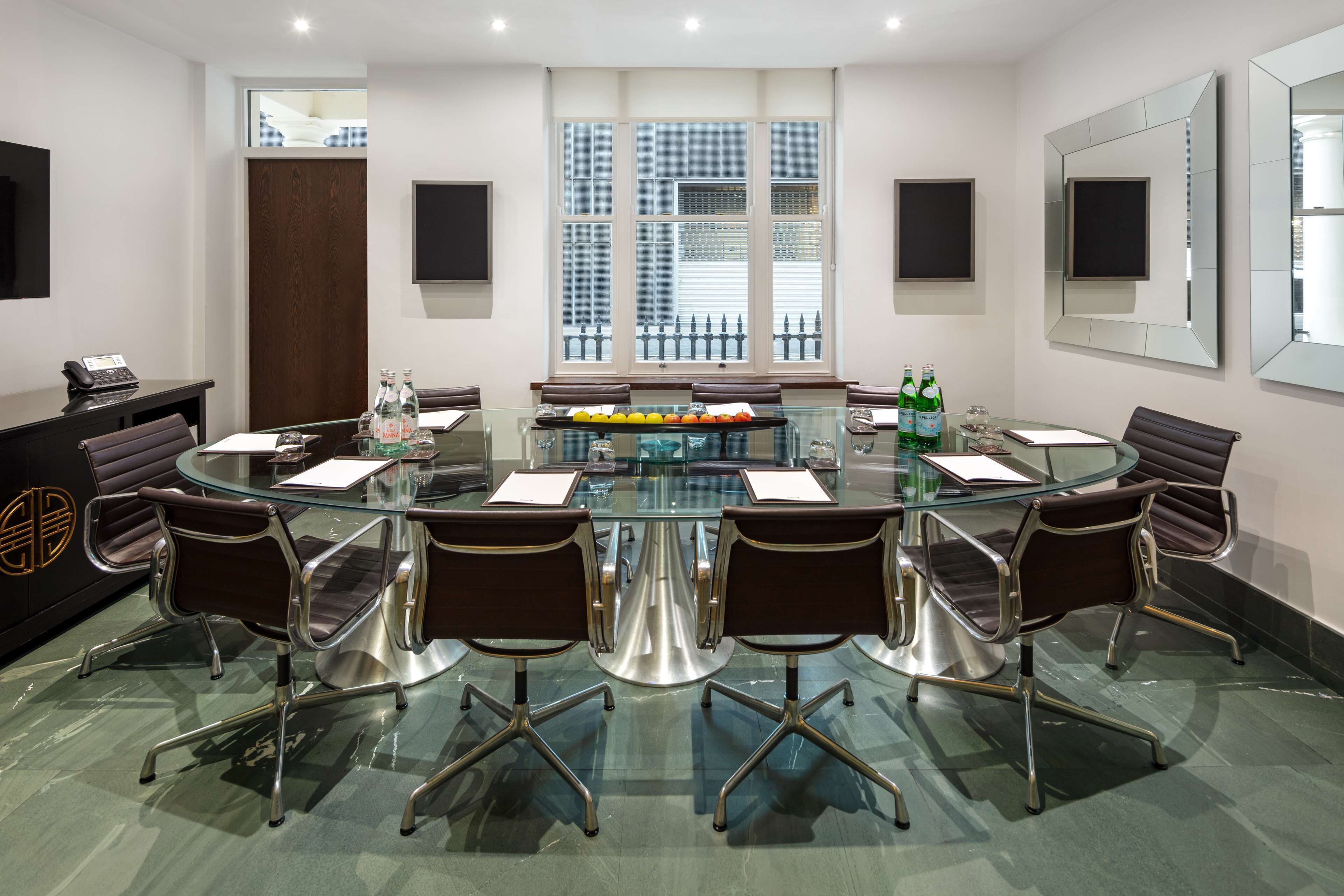 A conference room with a glass table, six chairs, a podium, and a large window with a view of a fence.