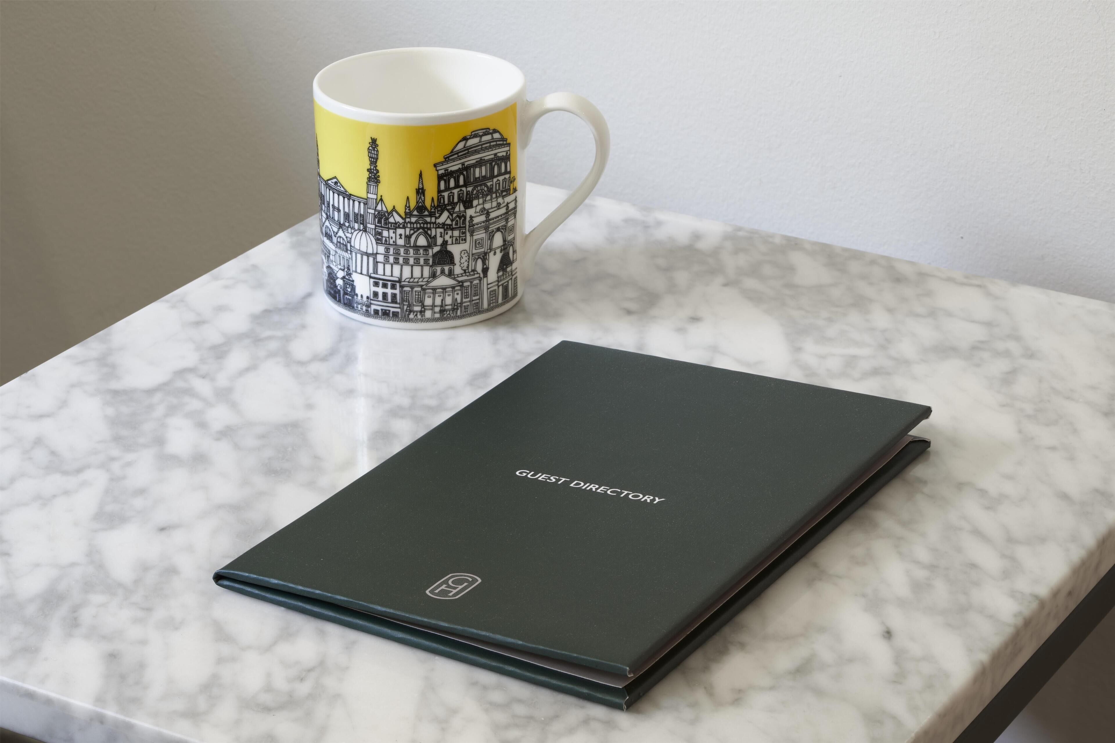 A marble table with a black guest directory and a mug with a cityscape design.