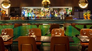A bar area with a well-stocked liquor display, seating with tables and chairs, and a green leaf-patterned backrest.