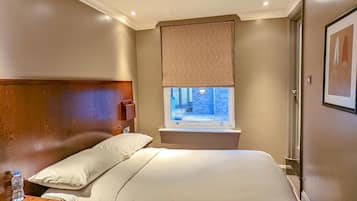 A hotel room with a large bed, a window with a view, a bedside table with a bottle, and a headboard.