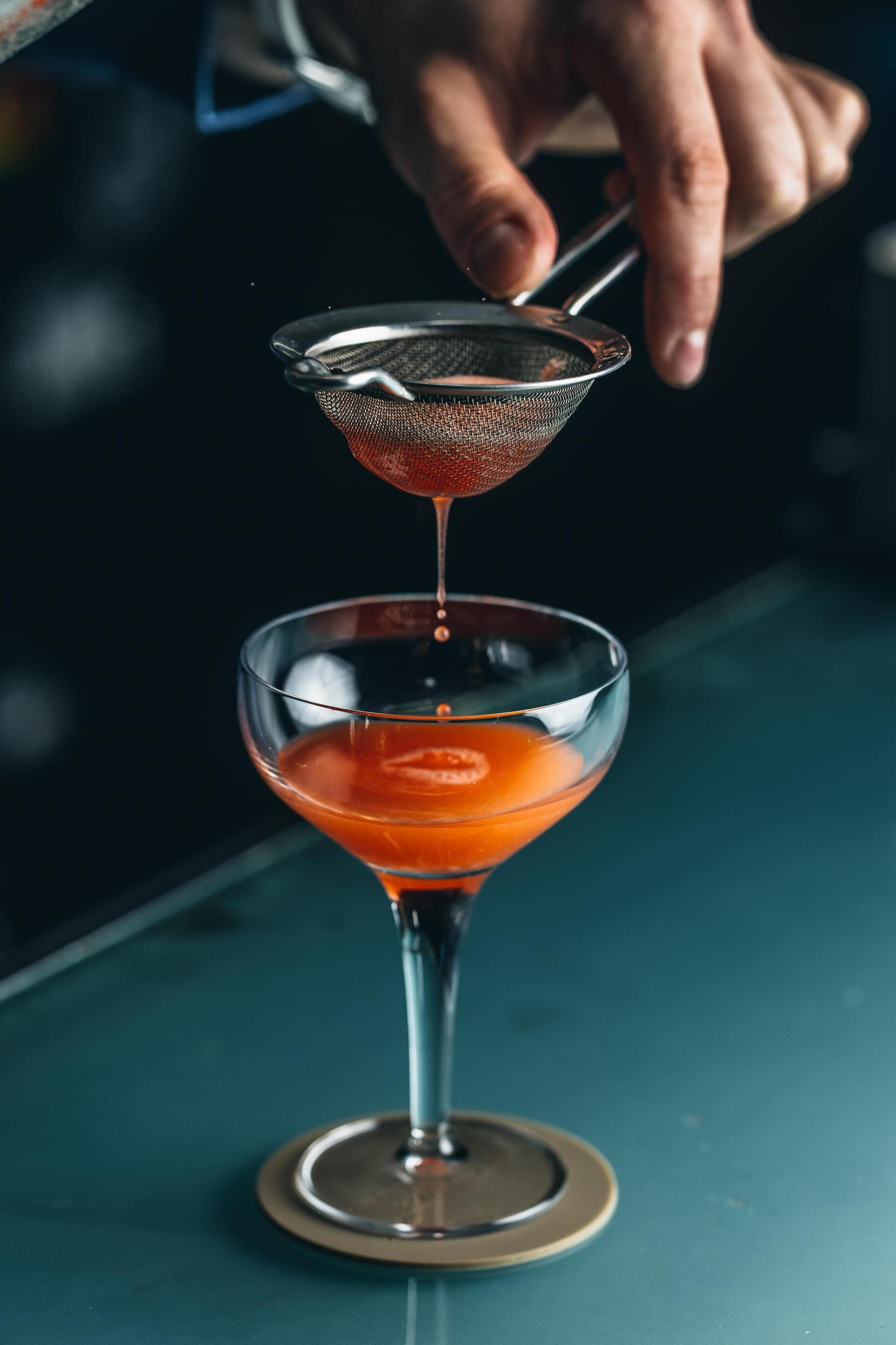 A hand pouring a drink into a martini glass.