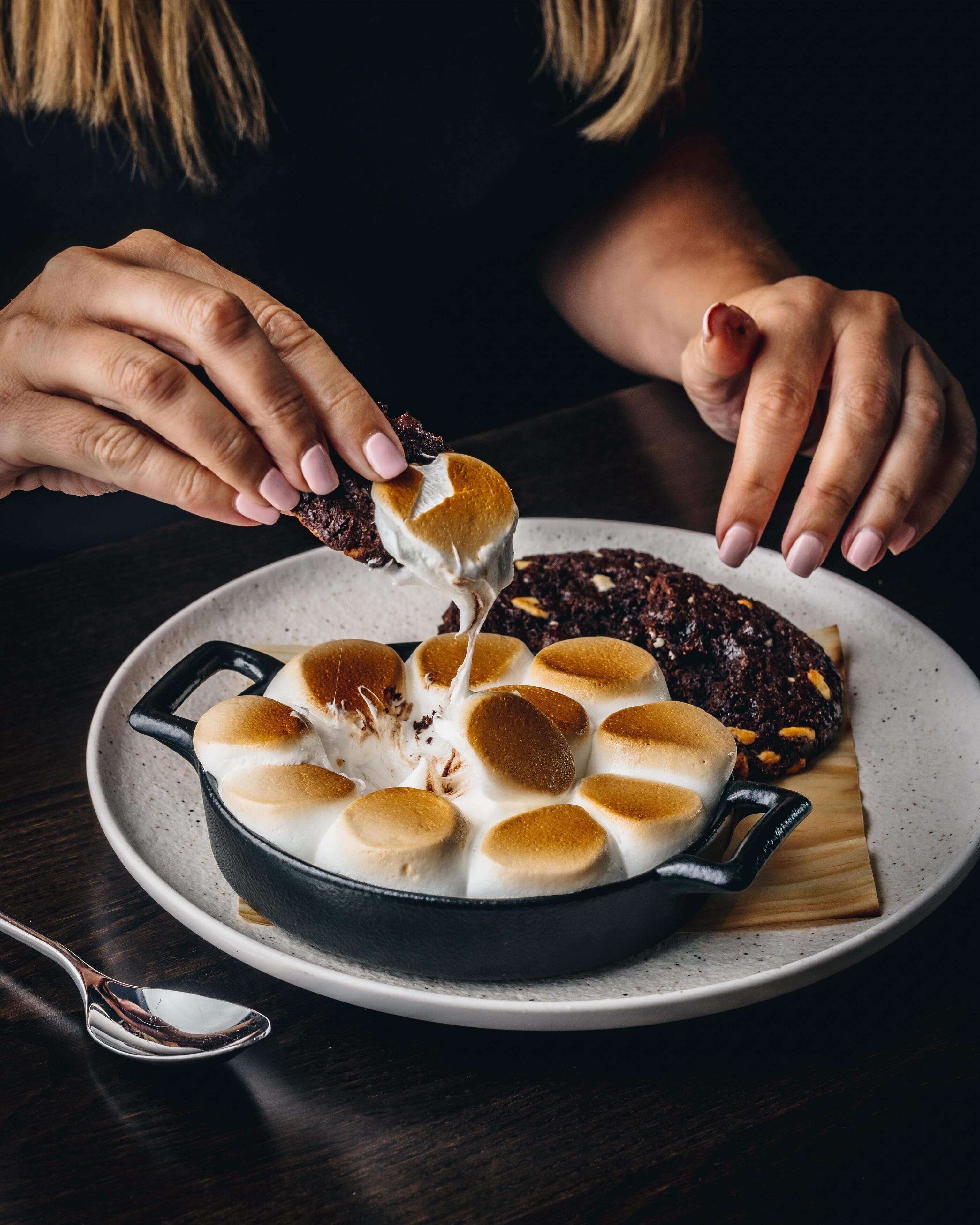 A person dipping a marshmallow into a pot of melted chocolate.