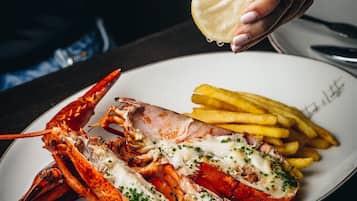 Una cola de langosta con salsa cremosa y cebollín, acompañada de papas fritas sobre un plato blanco.