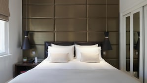 A neatly made bed with a headboard, two bedside lamps, and a nightstand with a plant and a bottle.
