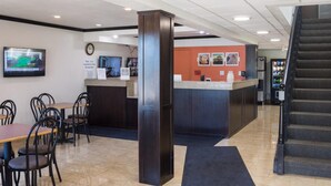 A hotel lobby with a reception desk, a clock, a television, and a staircase.