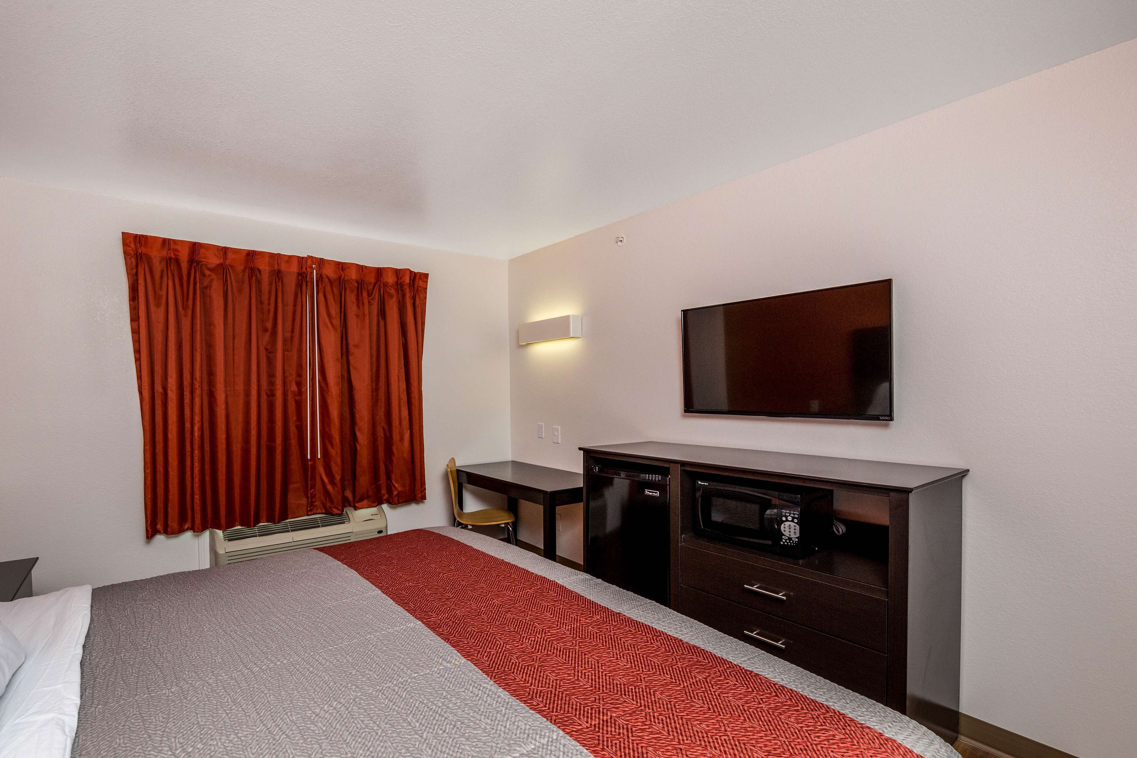 A hotel room with a bed, a desk, a chair, a TV, and a minibar.
