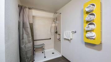 A wheelchair-accessible shower with a grab bar, a bench, and a yellow towel rack with towels.