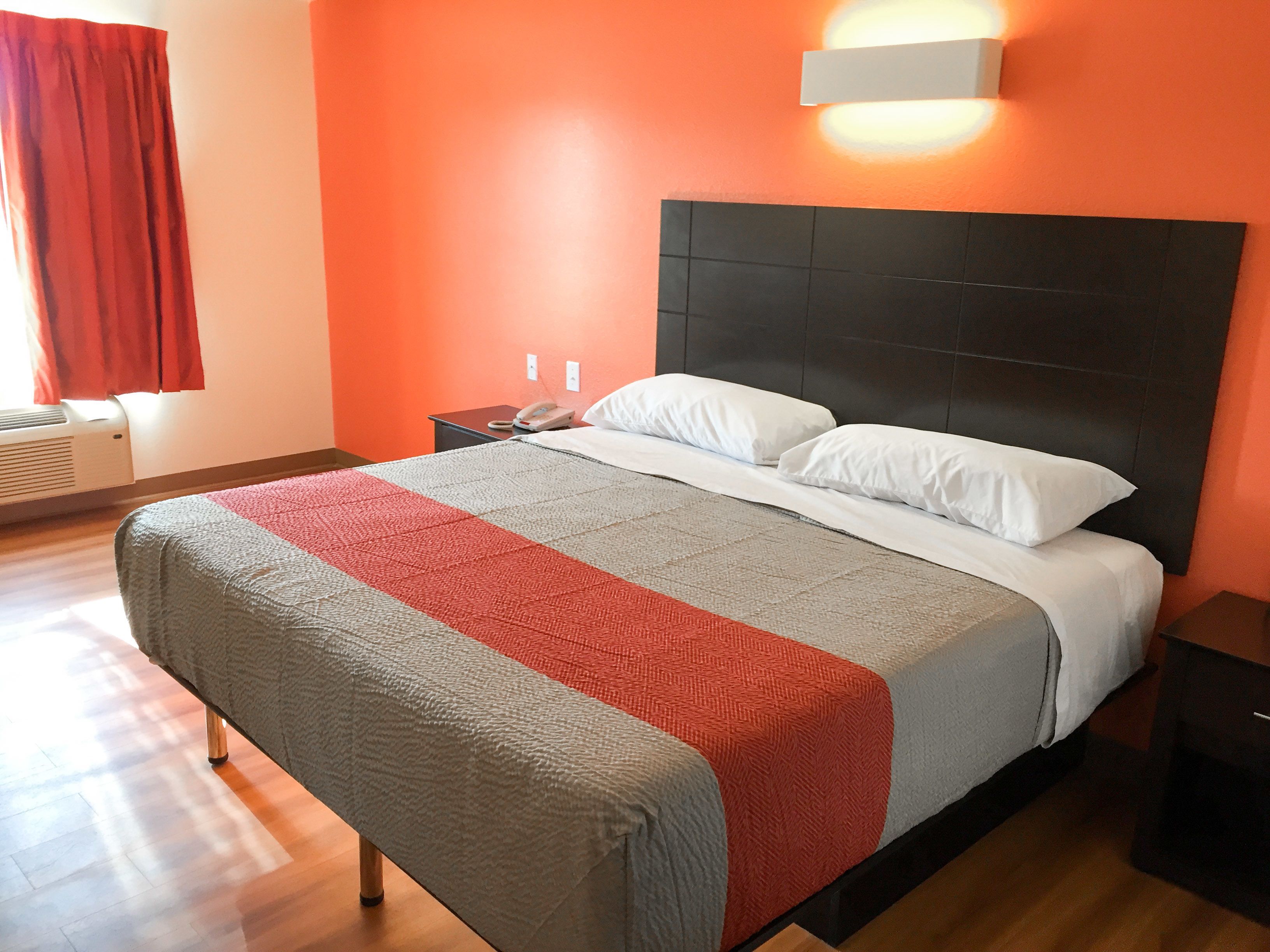 Een hotelkamer met een groot bed, een nachtkastje, een telefoon en een wandlamp.