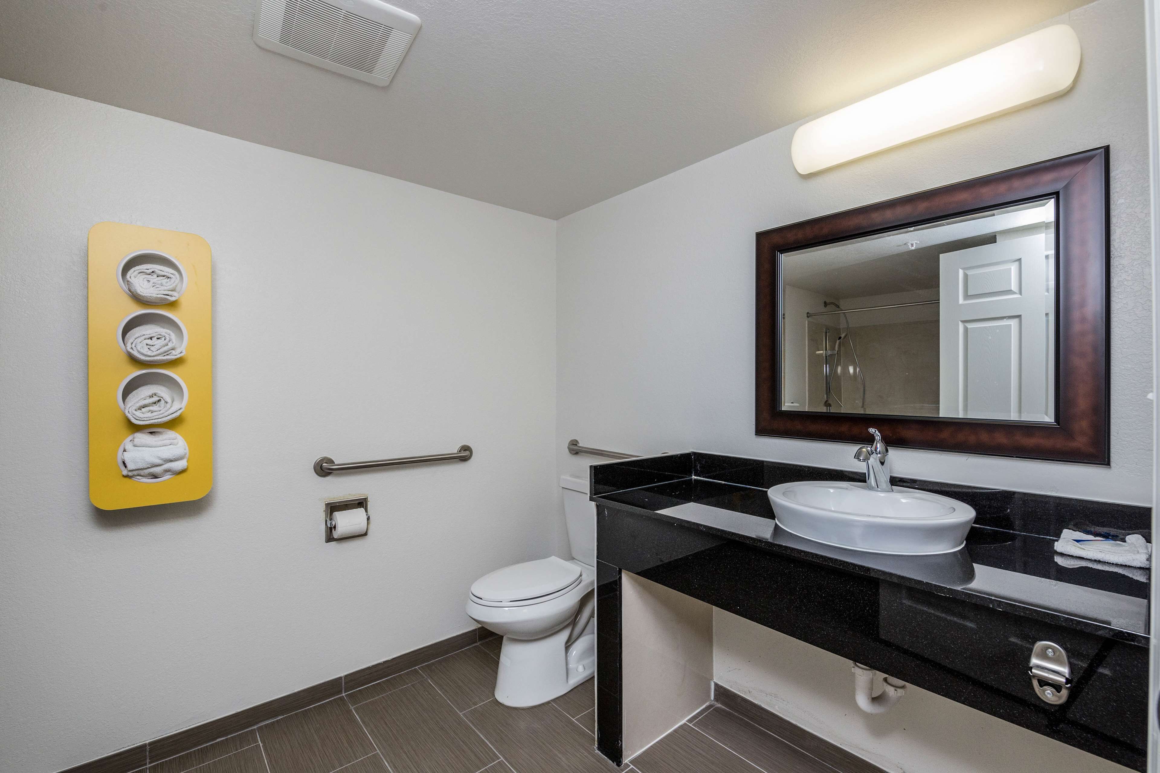 Un baño con inodoro blanco, lavamanos con espejo y toallero amarillo con toallas.