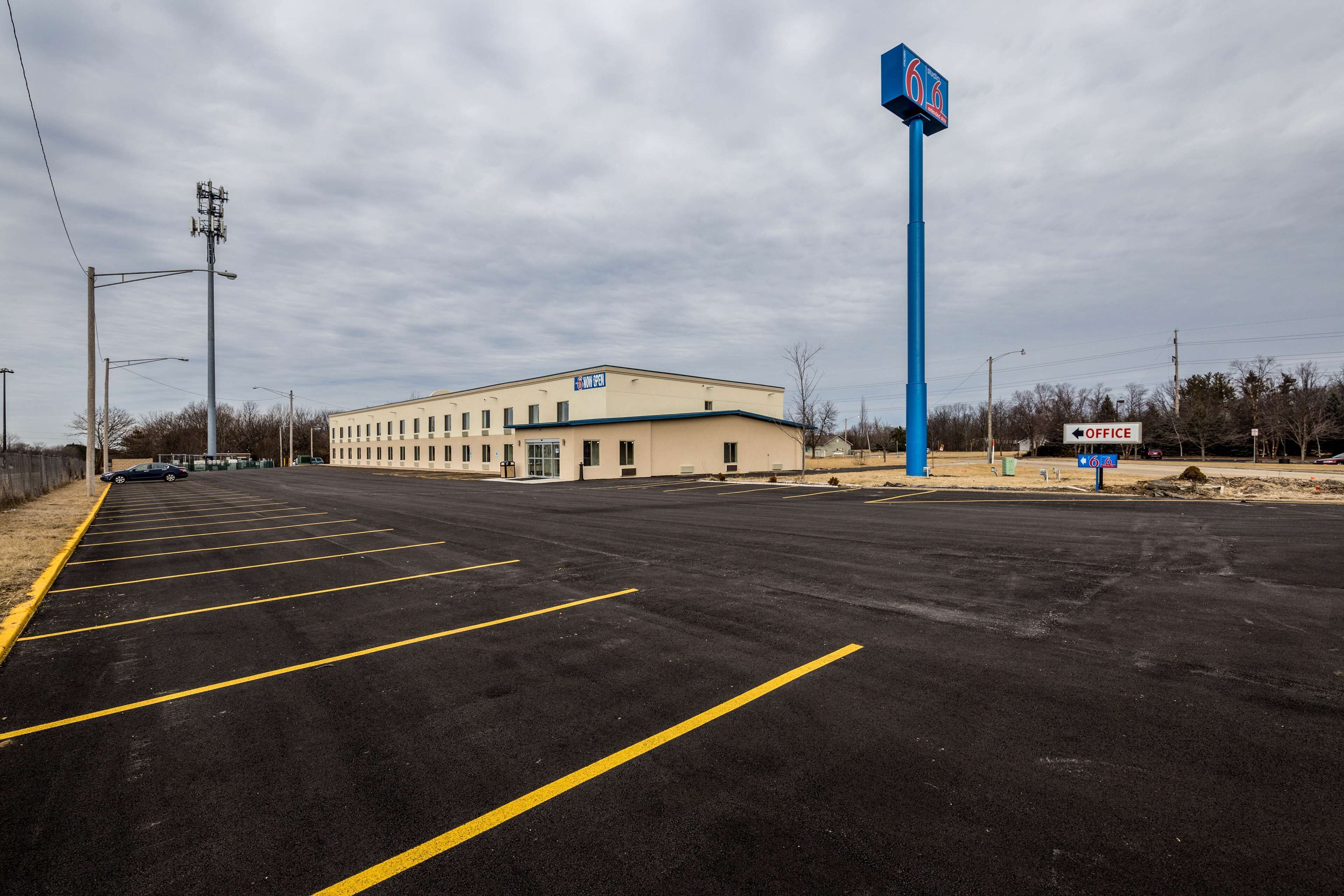 A parking lot with marked spaces, a building with a sign indicating an office, and a blue sign with a logo.