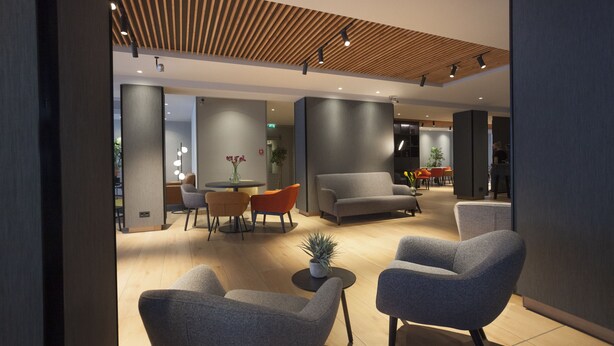 A modern interior with a wooden ceiling, grey sofas, a round table, and a potted plant. - ibis Styles Den Haag Scheveningen (The Hague)