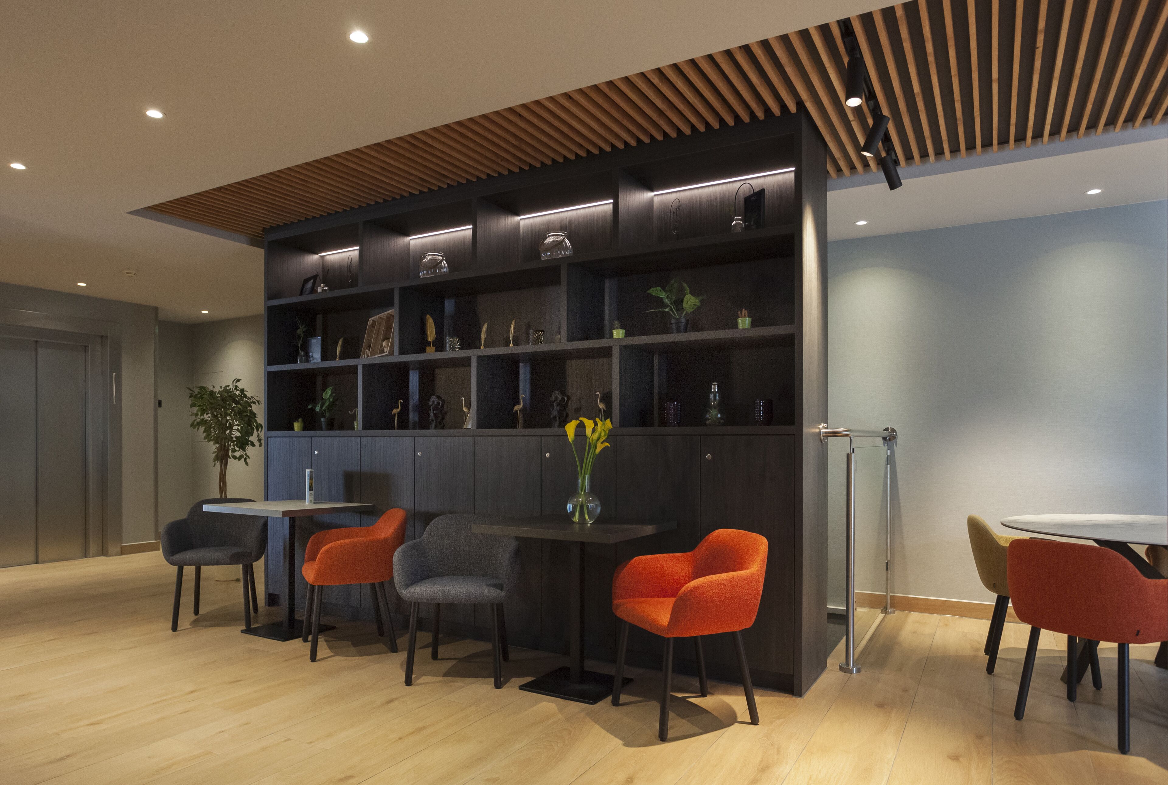 A modern interior with a dark wood panel ceiling, a built-in bookshelf, and a seating area with a table and chairs.