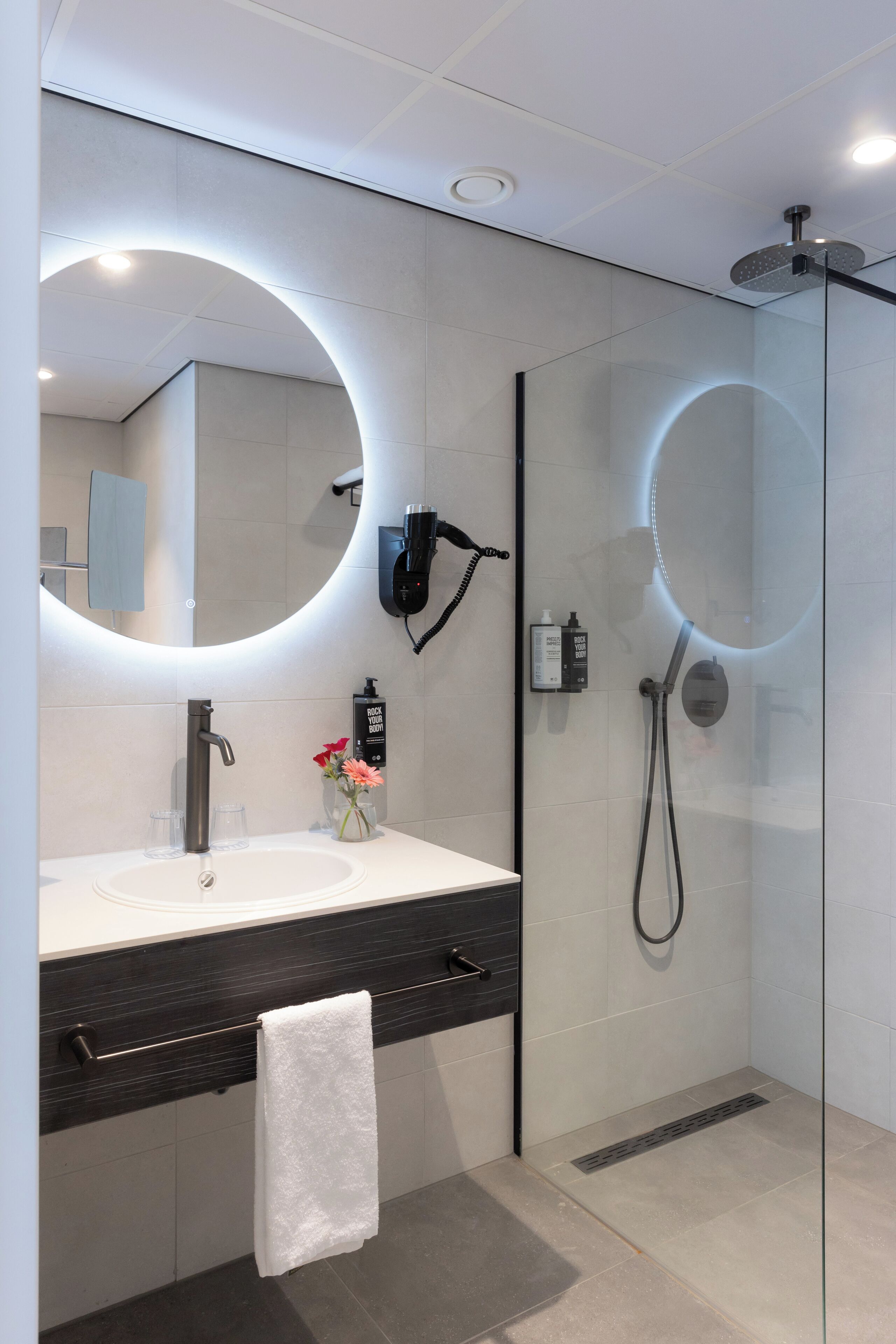 A modern bathroom with a glass-enclosed shower, a round mirror, a white sink, and a black countertop.