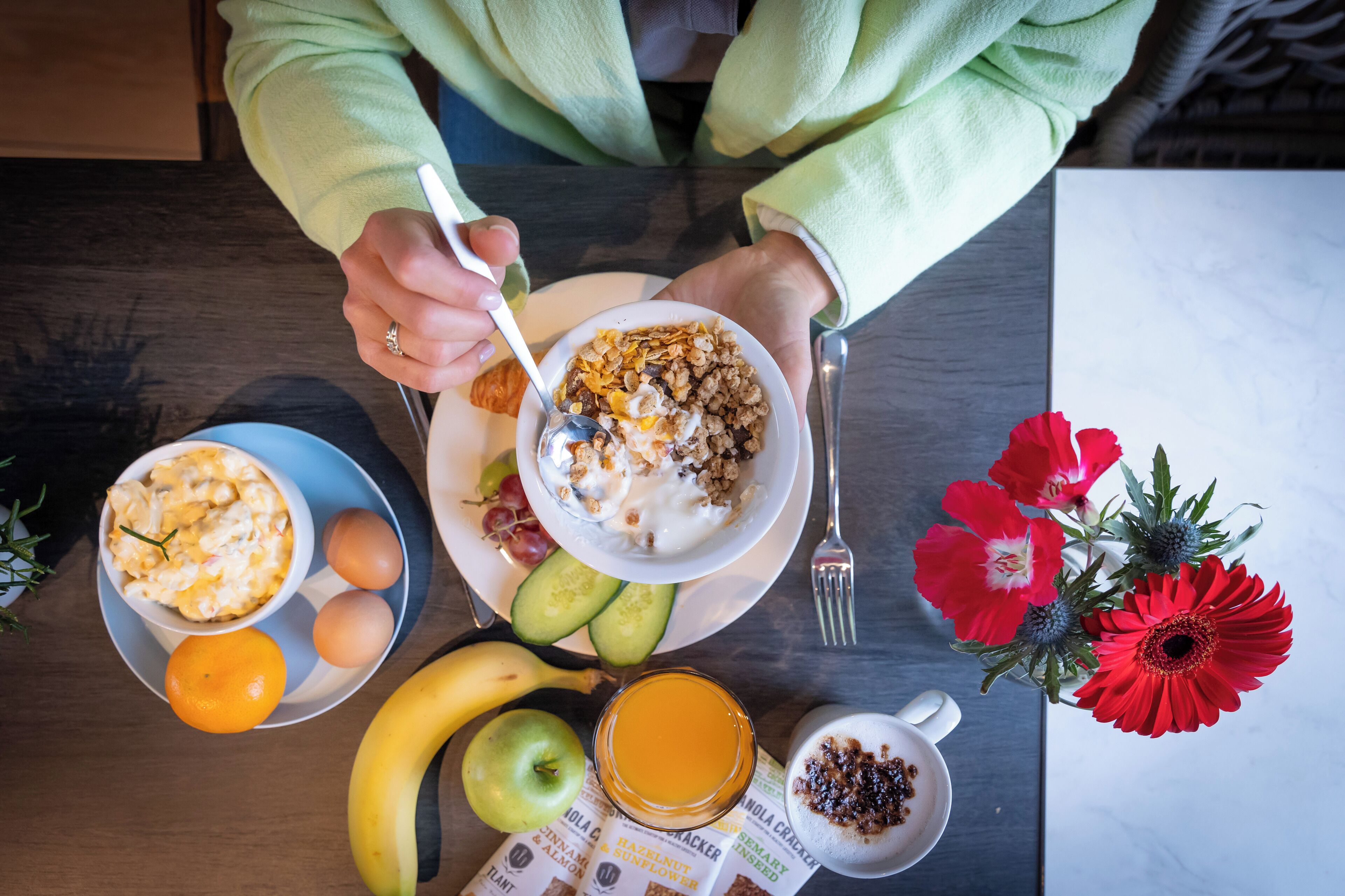 Een ontbijttafel met een kom cornflakes, eieren, een banaan, een sinaasappel en een glas sinaasappelsap.