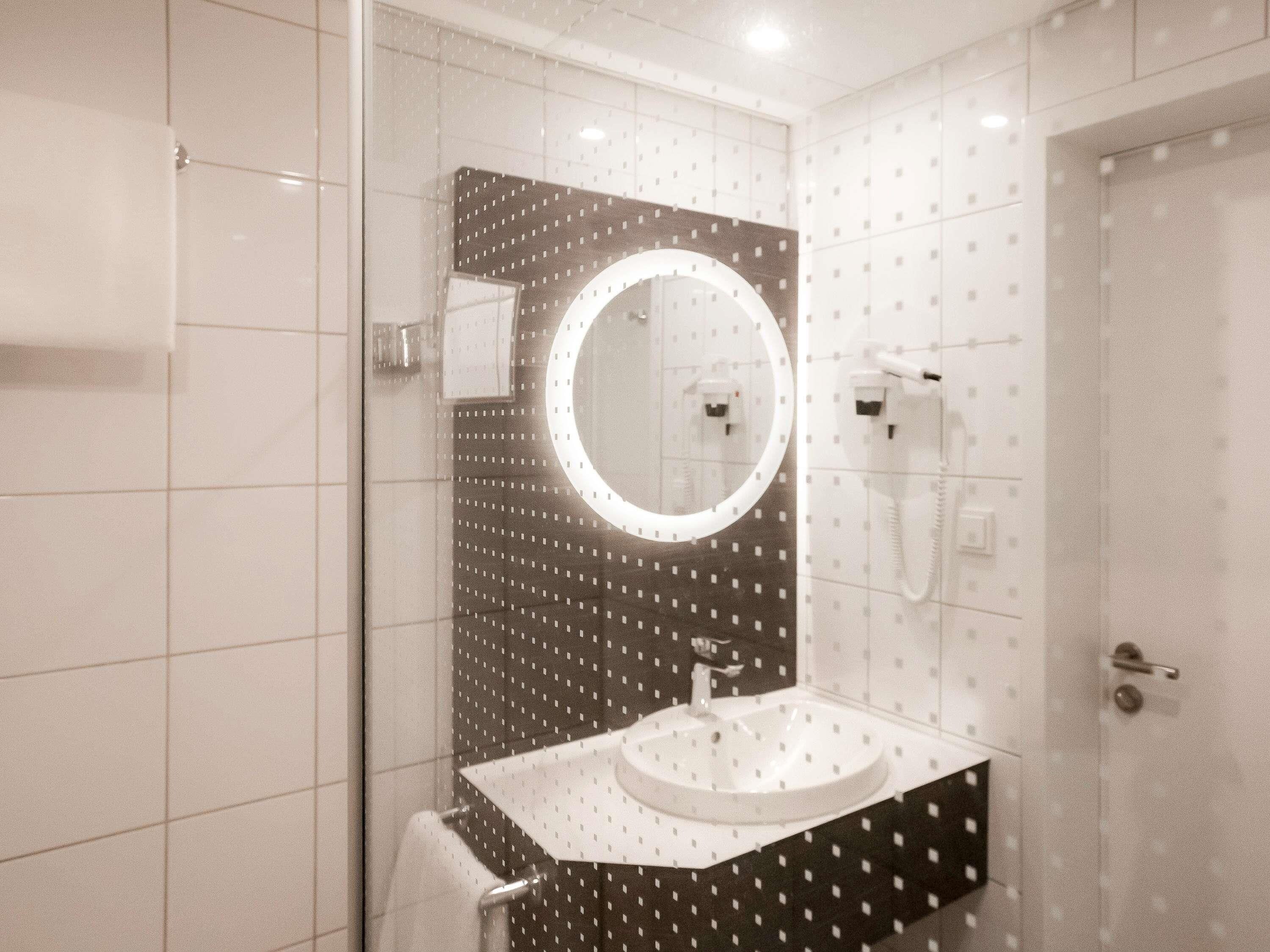 A modern bathroom with a round mirror, a sink, and a hairdryer mounted on the wall.