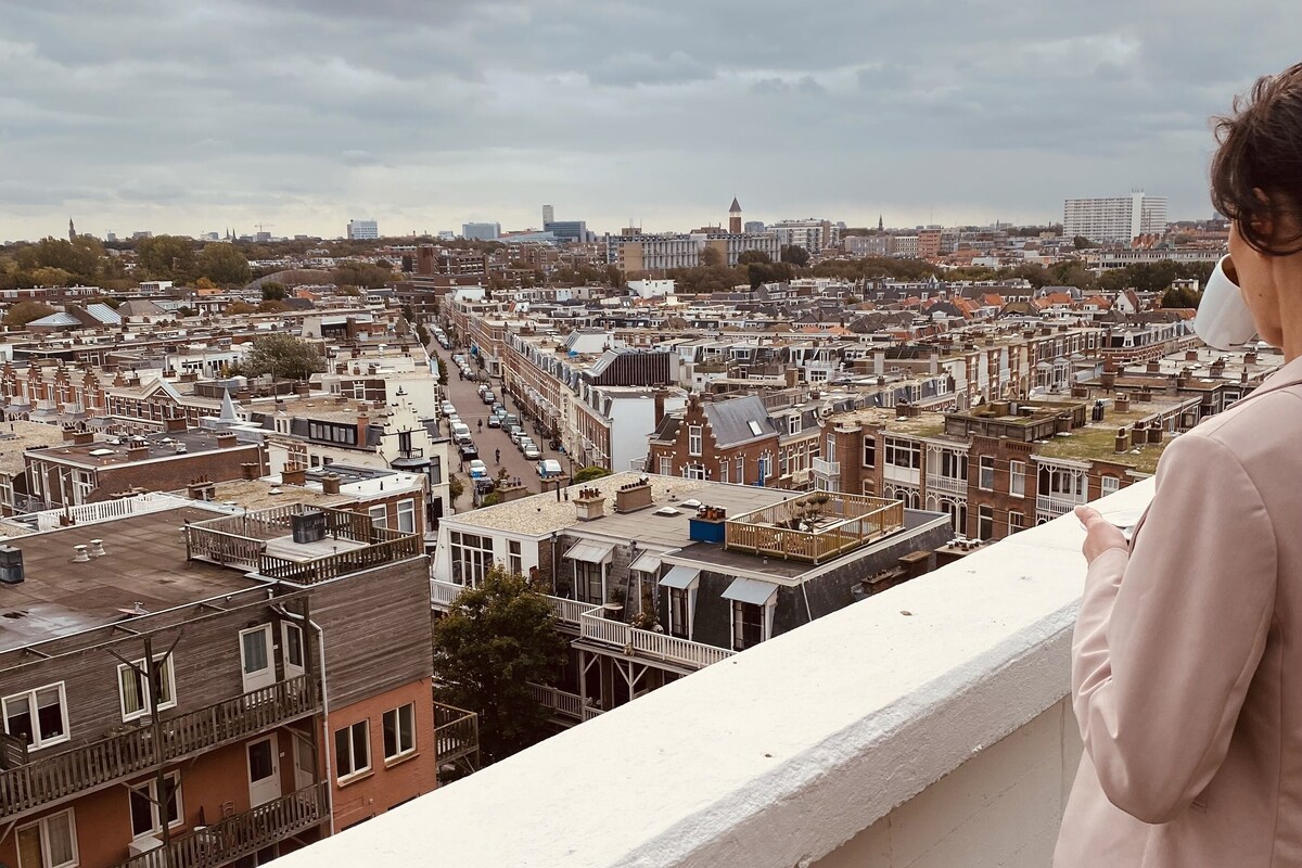 A balcony overlooking a densely packed urban area with various buildings and a cloudy sky.