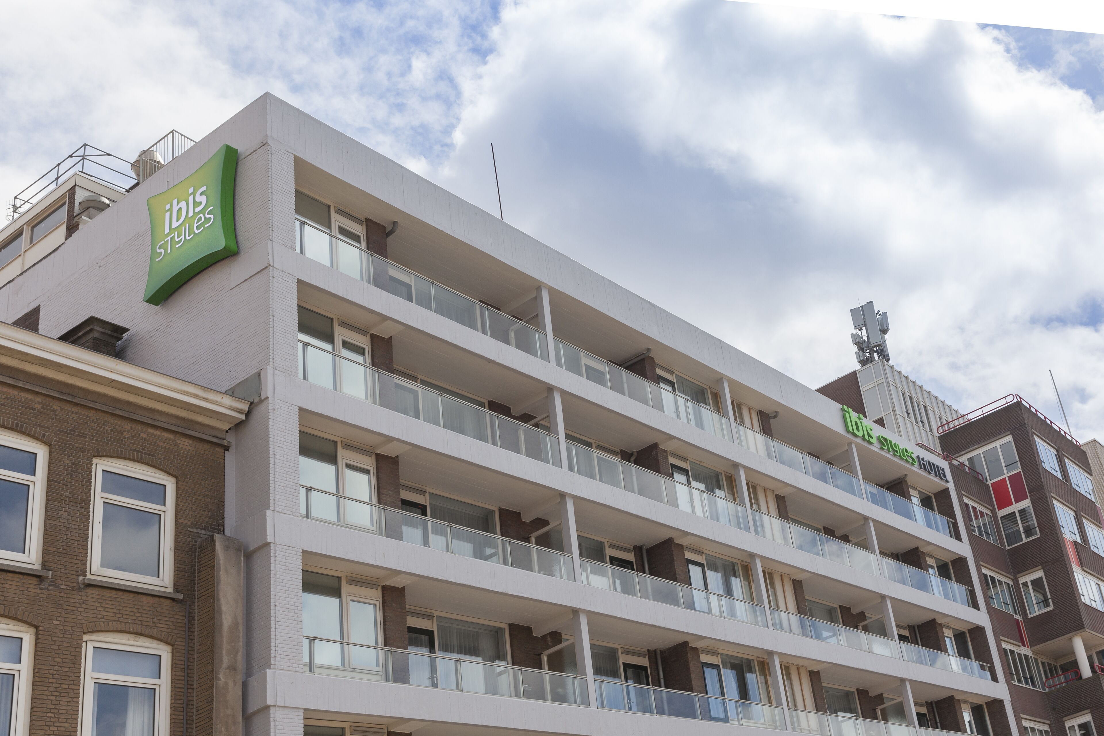 Un hotel de varios pisos con balcones, un cartel verde destacado y una vista despejada del cielo.