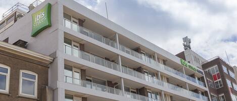 Un hotel de varios pisos con balcones, un cartel verde destacado y una vista despejada del cielo.