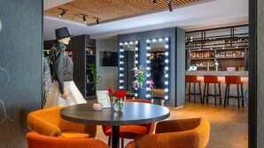 A modern interior with a round table, orange chairs, a bar area with stools, and a mannequin in a black outfit. - ibis Styles Den Haag Scheveningen (The Hague)