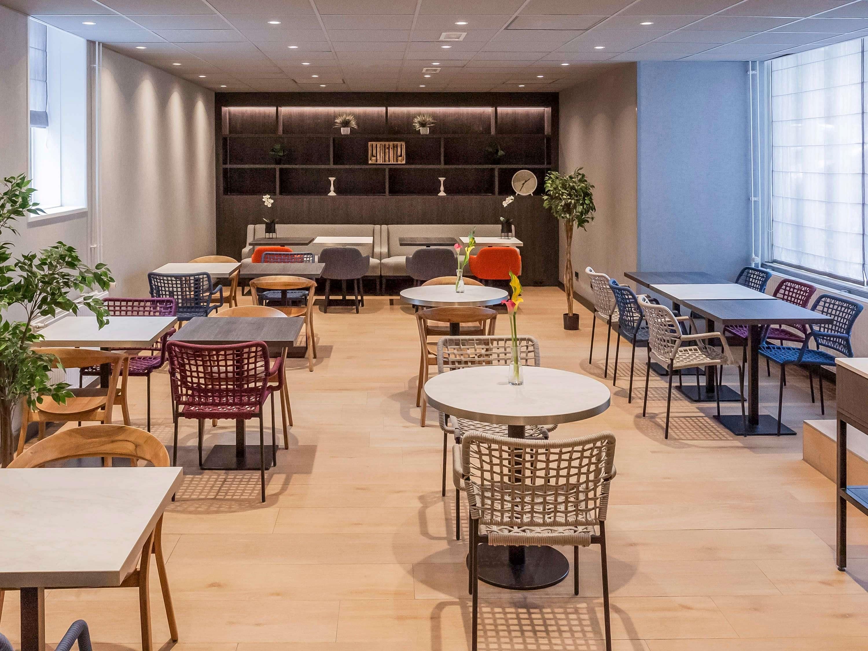 A modern cafe with round tables, wicker chairs, and potted plants.