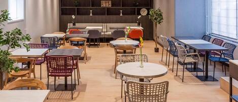 A modern cafe with round tables, wicker chairs, and potted plants.