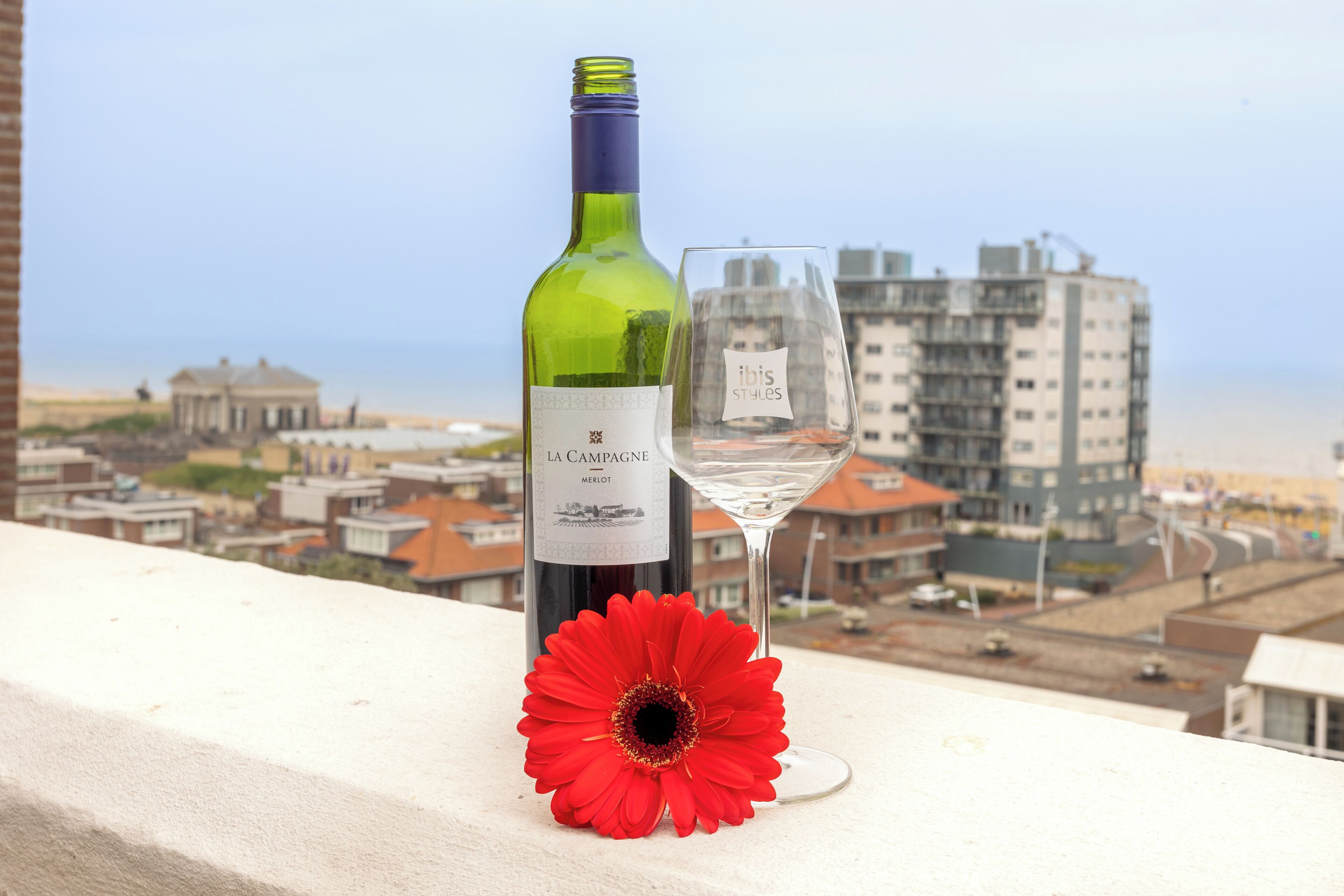 A bottle of wine and a glass on a balcony with a cityscape view.