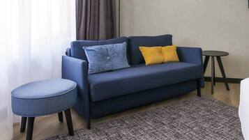 Una sala de estar moderna con un sofá azul oscuro, dos cojines, un otoman redondo, una alfombra estampada, una mesita redonda y una lámpara de pie.