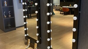 Two tall mirrors with light bulbs, placed on a wooden floor in a room with a modern interior design. - ibis Styles Den Haag Scheveningen (The Hague)