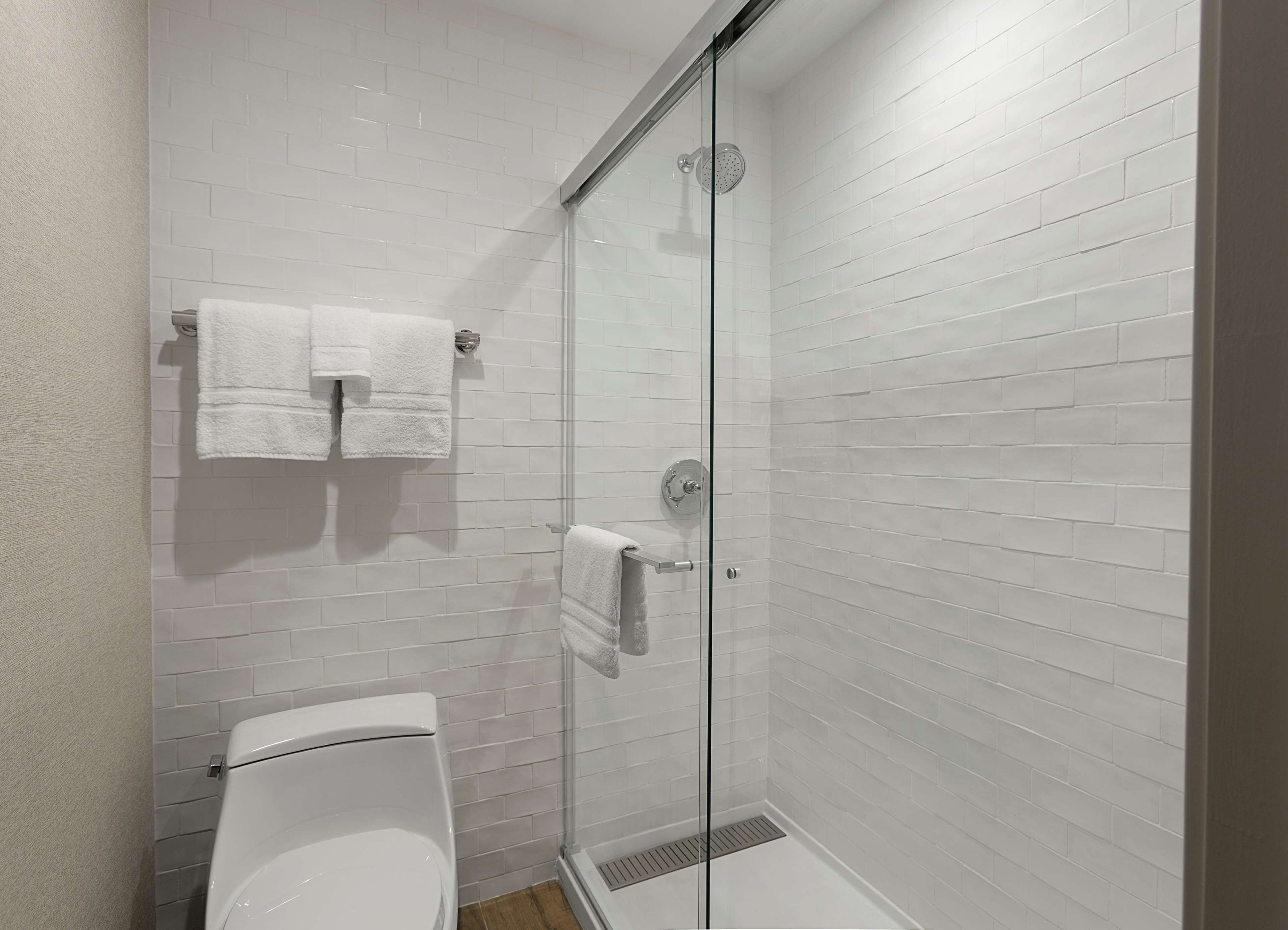 Un baño moderno con azulejos blancos tipo metro, mampara de vidrio y un inodoro.