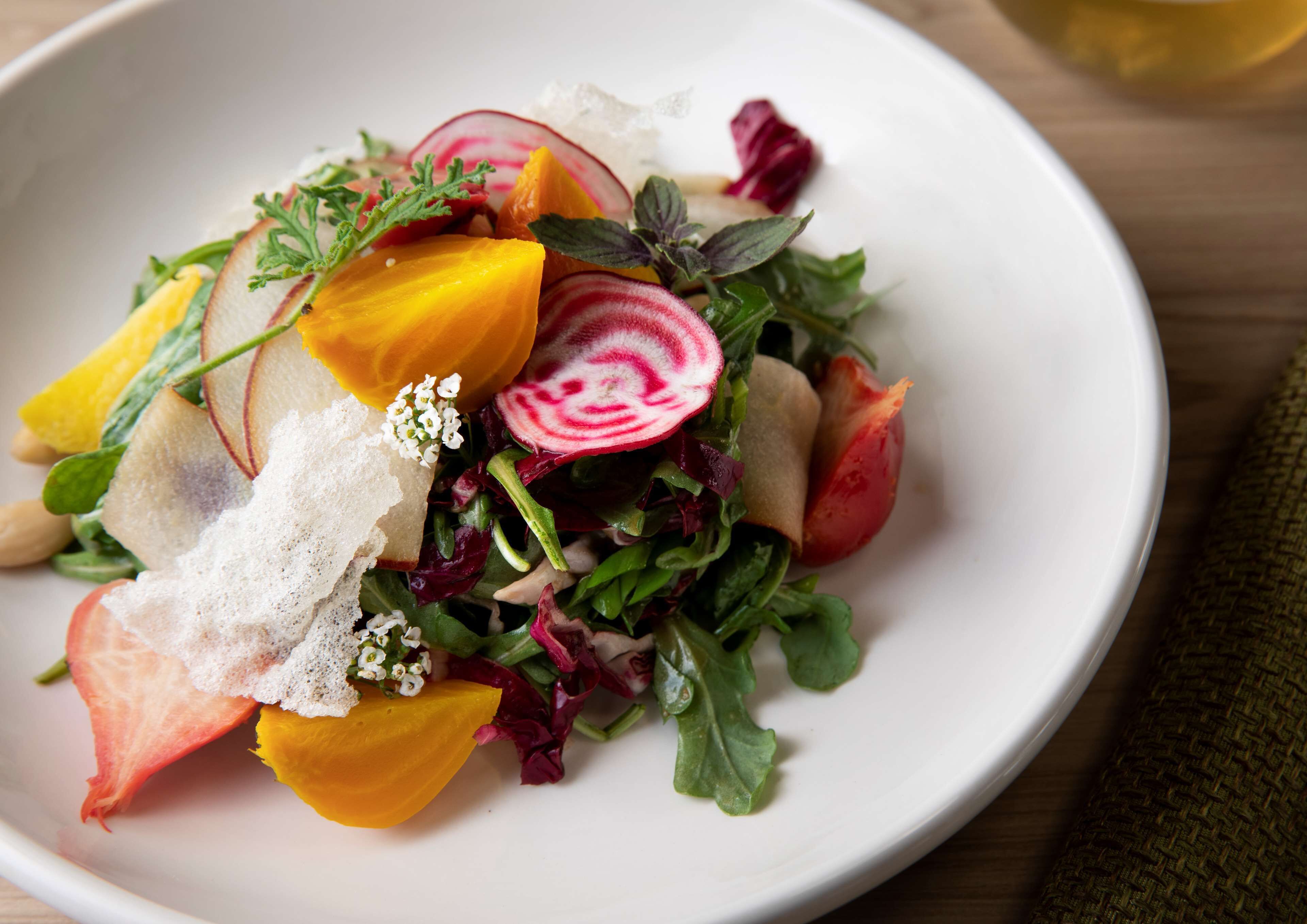Un plato blanco con una ensalada que incluye diversas verduras y frutas.