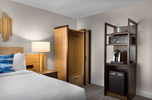 A hotel room with a bed, bedside lamp, wooden wardrobe, and a built-in mini-fridge. - Sonesta Silicon Valley (Milpitas)