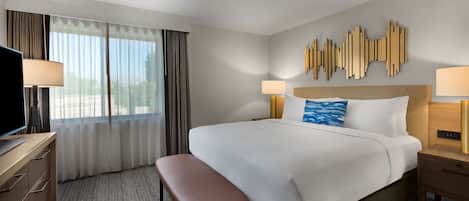 A hotel room with a large bed, a desk with a television, and a window with curtains.