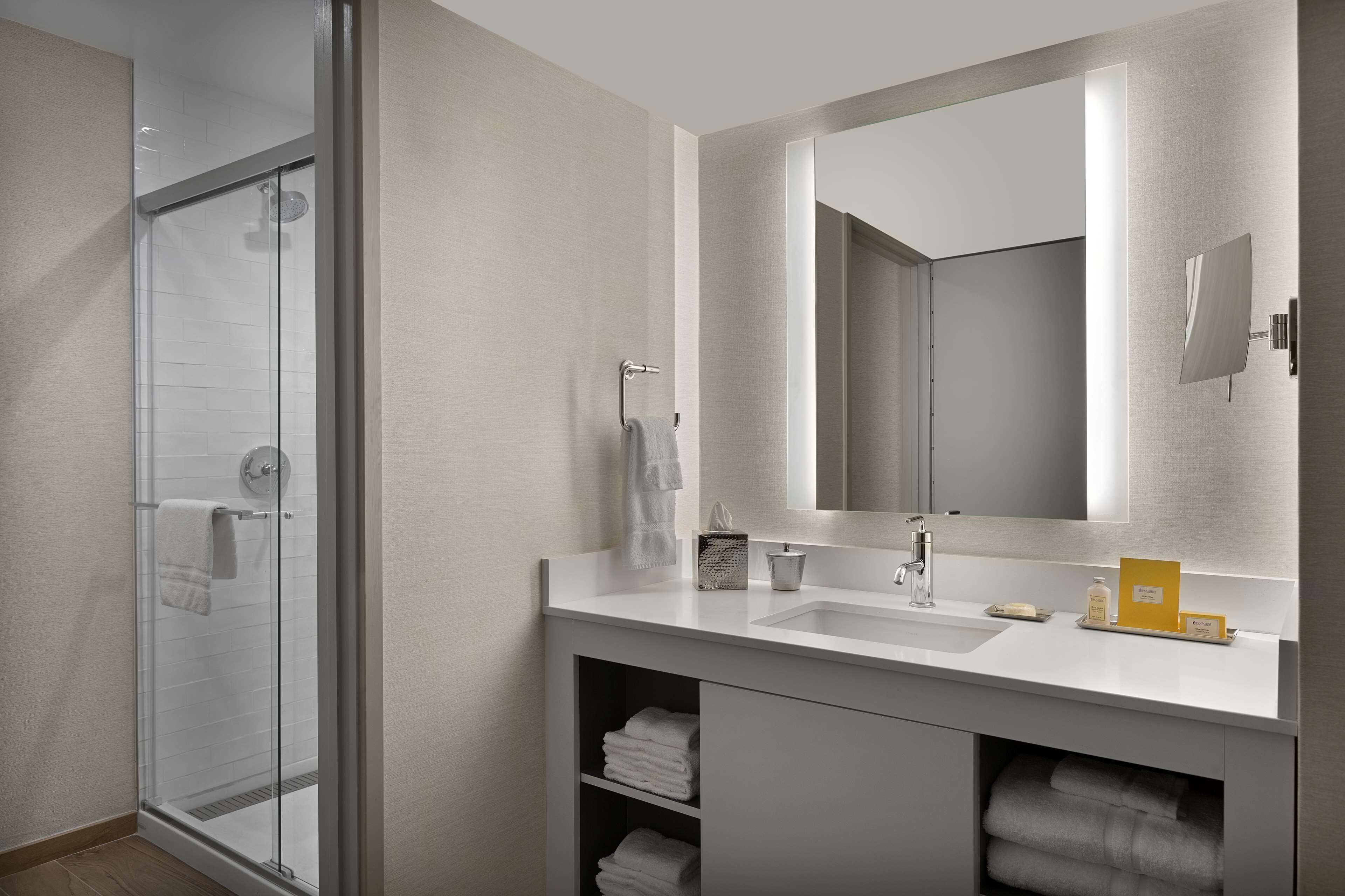 A modern bathroom with a glass shower enclosure, a large mirror, and a white vanity with a sink and towel storage.