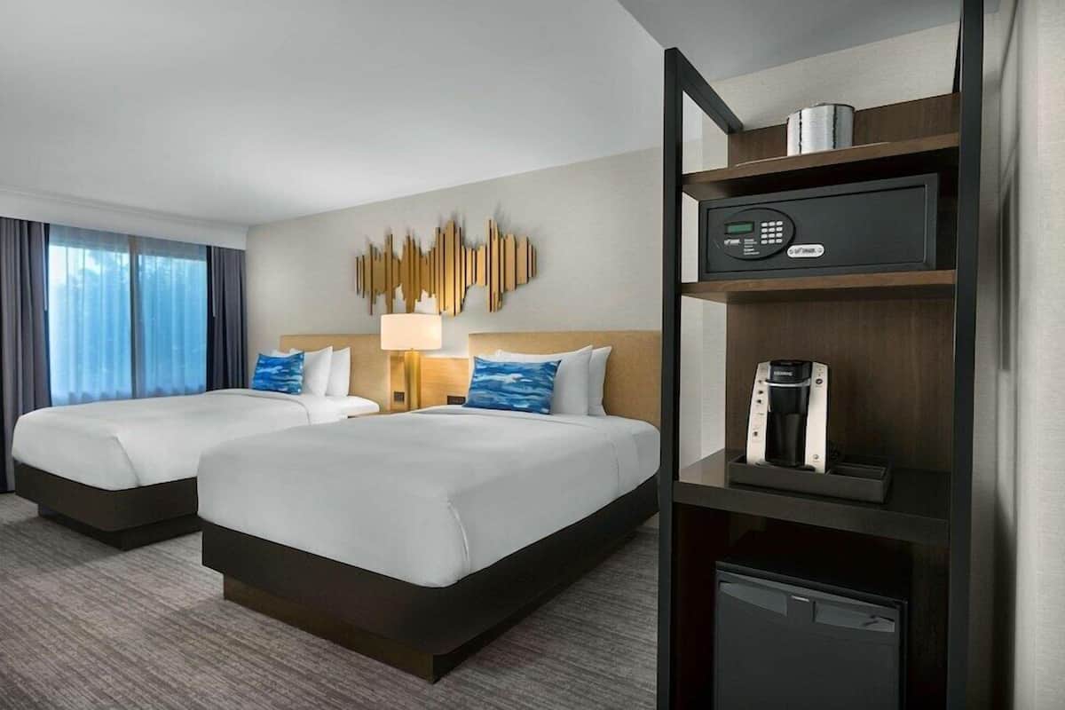 A hotel room with two beds, a wall-mounted TV, a coffee machine, and a minibar.